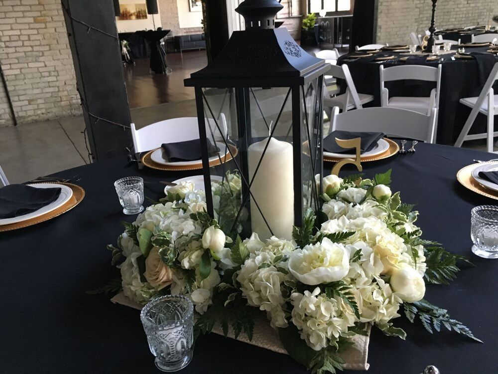 Centerpiece: Black lantern with candle on white floral arrangement, black tablecloth.