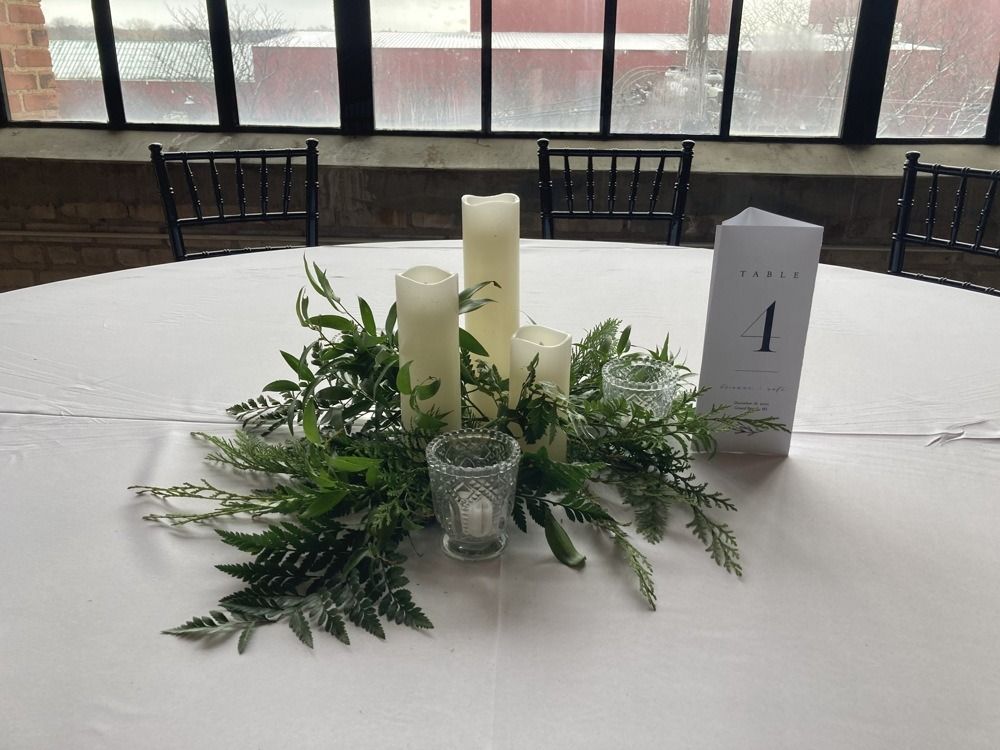 Centerpiece on a white tablecloth with candles, greenery, and a table number 1.