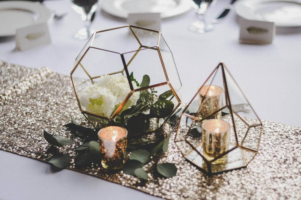 Gold geometric terrariums with candles and flowers on a sparkly gold table runner.