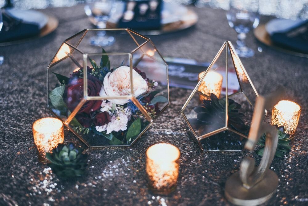 Geometric glass terrariums with flowers and candles on a glittery table.