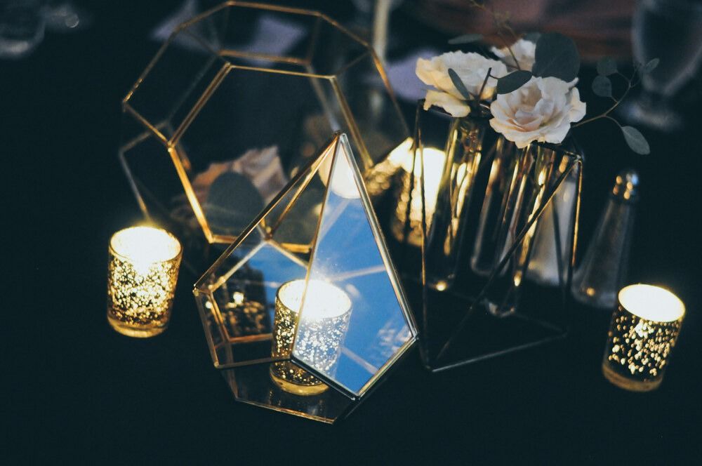 Centerpiece with gold geometric glass, candles, and white flowers. Dark table setting.