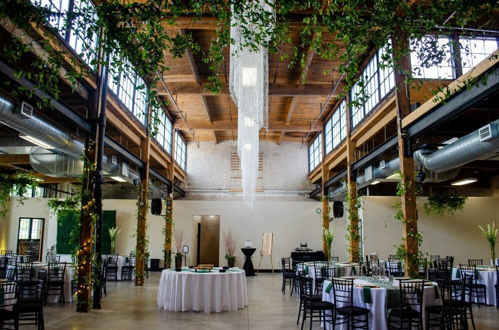 Spacious event hall with high ceilings, exposed beams, string lights, and tables set for a gathering.