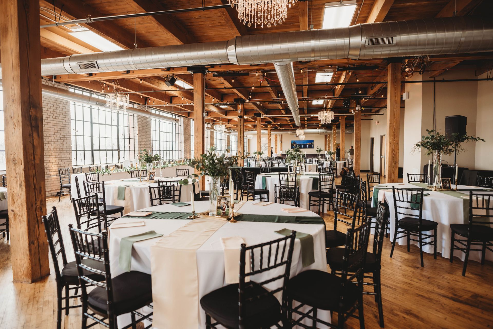 Wedding reception in industrial loft; round tables with white linens, black chairs, and floral centerpieces.