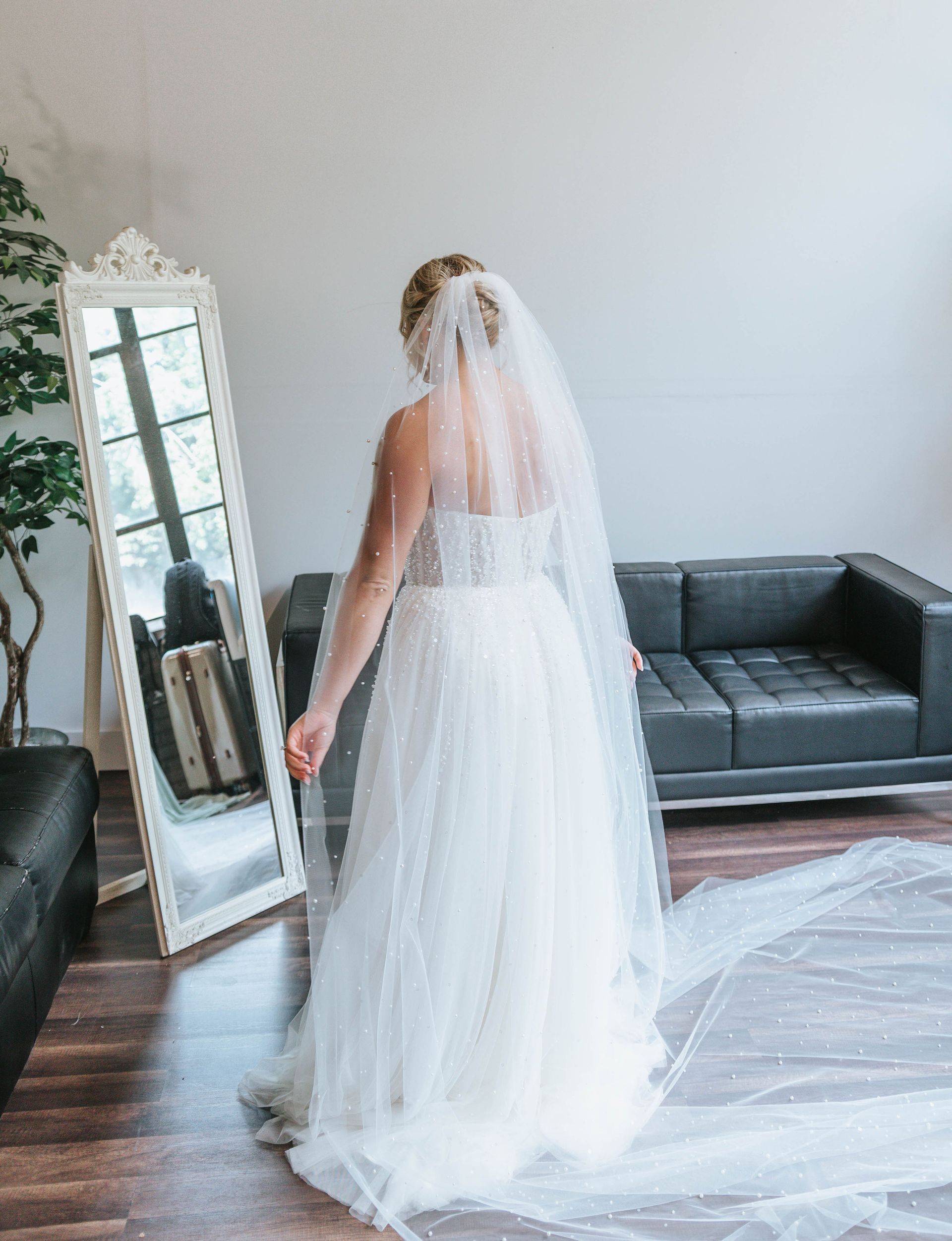 Bride in white wedding dress with veil, looking in a mirror.