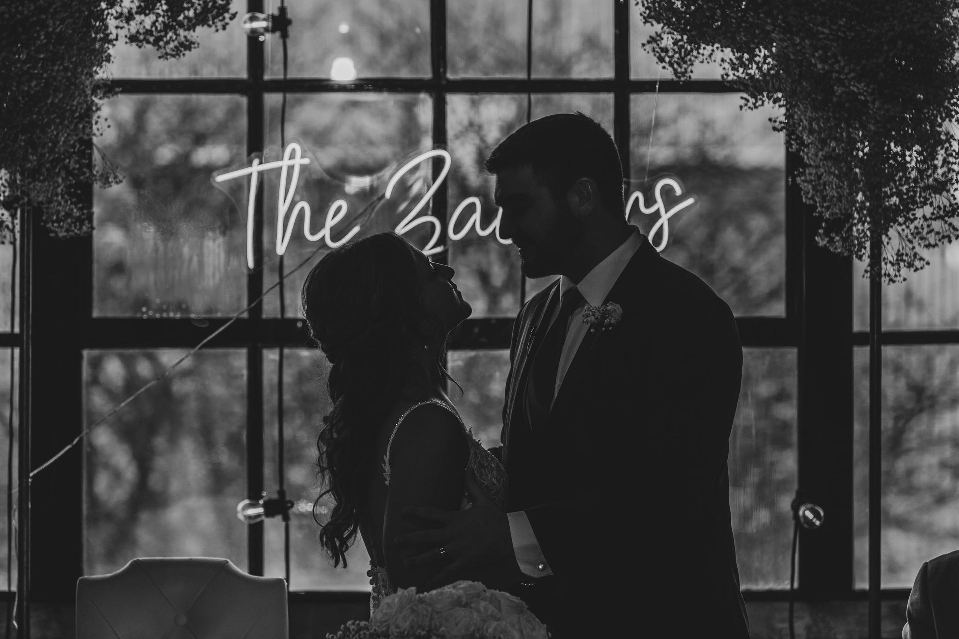 Newlyweds embrace in front of a neon sign that says 