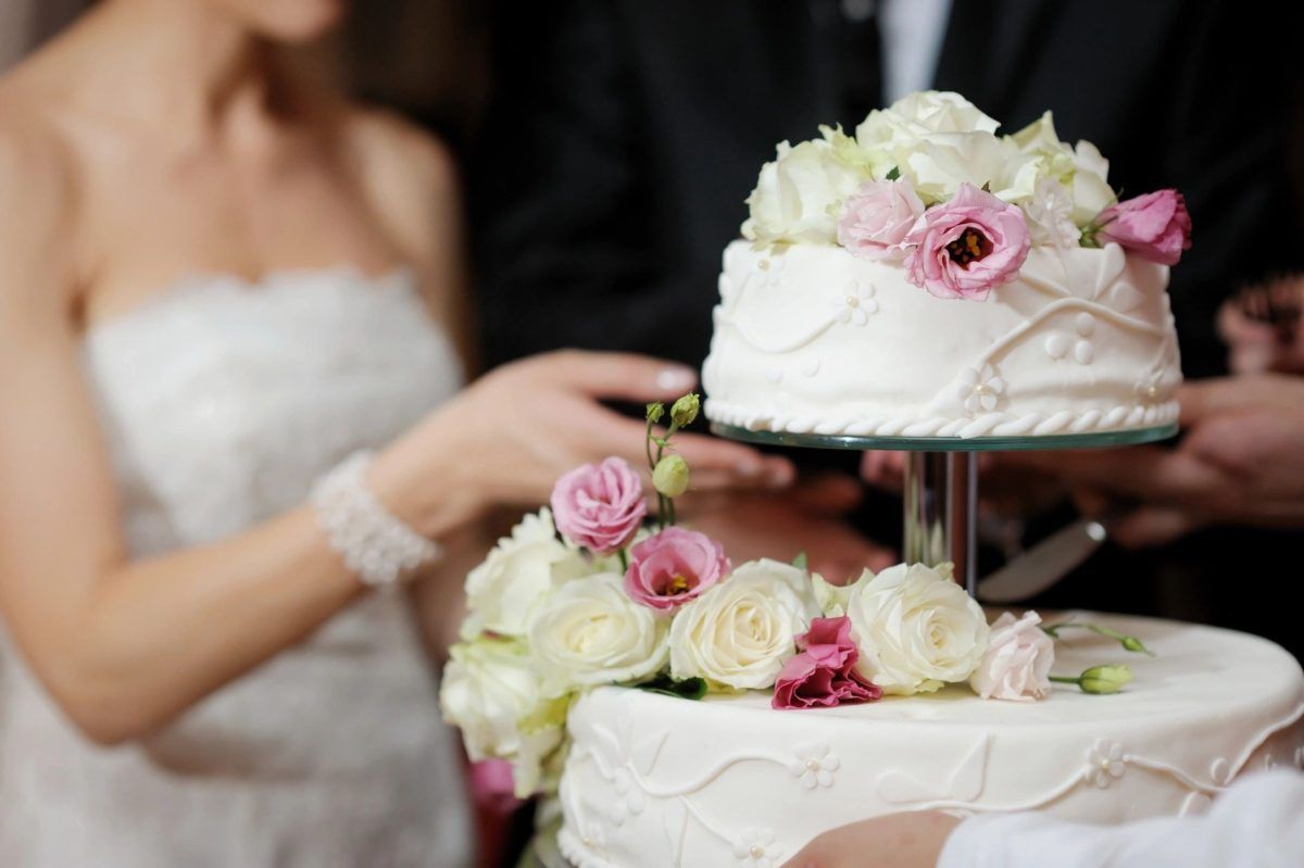 Bride and groom cutting a tiered wedding cake decorated with flowers.