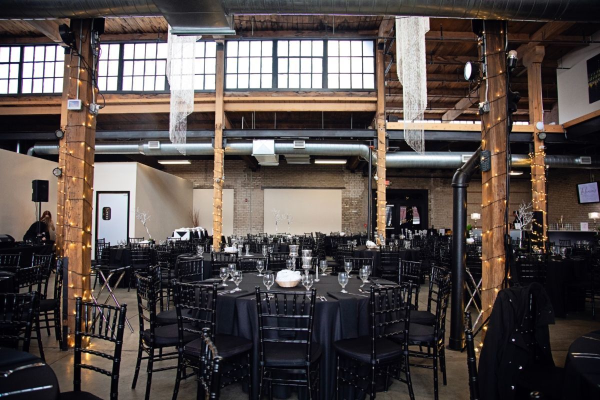 Event space with black tables and chairs, wood beams, and string lights.