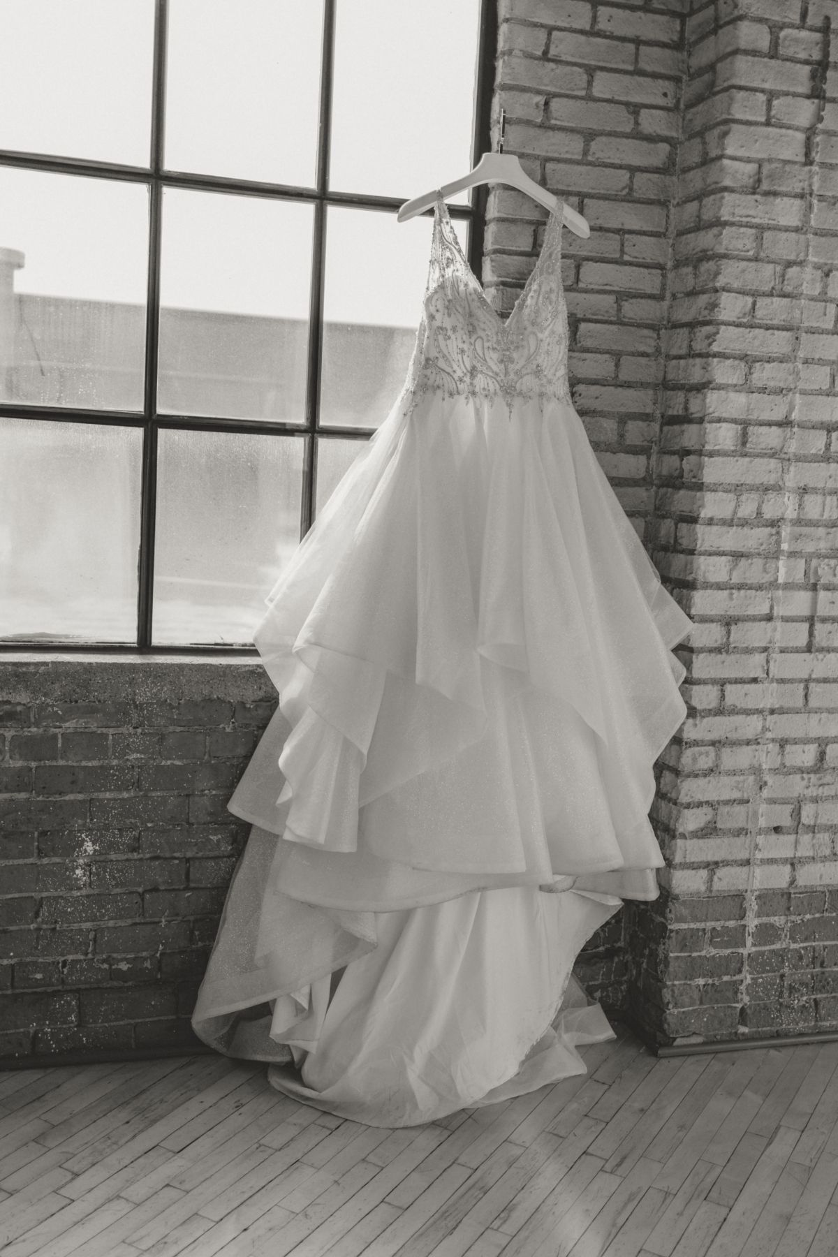 Wedding dress hanging by a window in a brick-walled room.