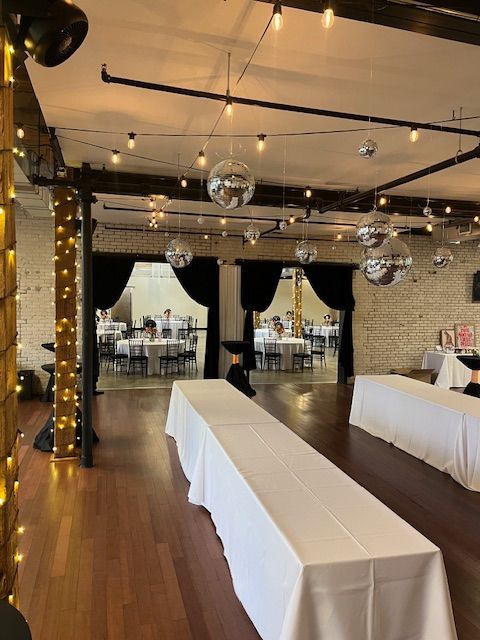 Event space with tables, string lights, and disco balls; room opens to another with tables.