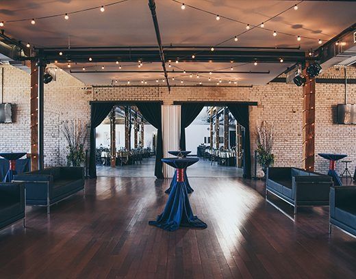 Elegant event space with dark blue couches, tables with blue cloths, and exposed brick walls.