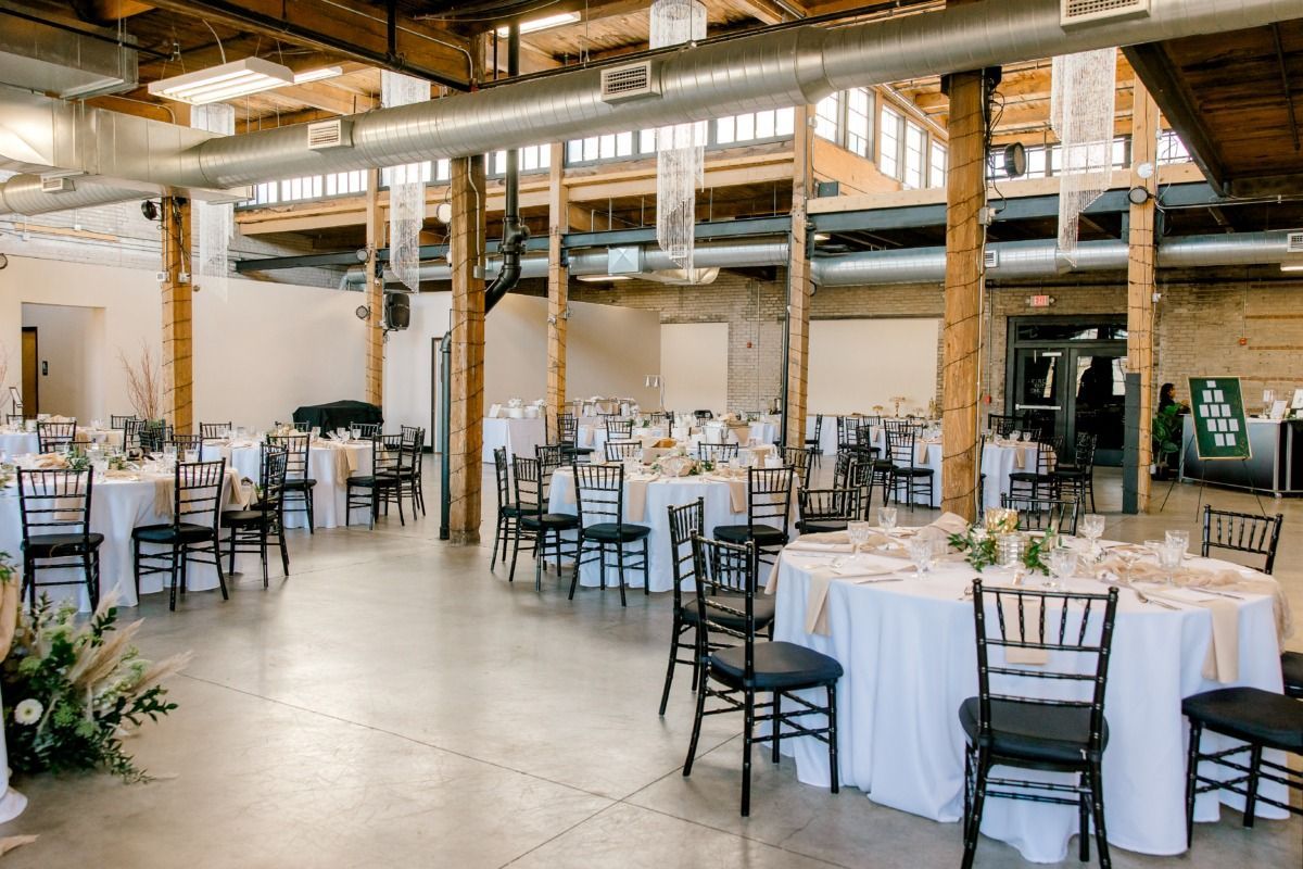Empty event space set for a reception; white tablecloths, black chairs, and wooden beams.