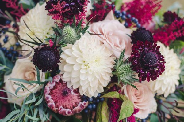Close-up of a bridal bouquet with white dahlias, pink roses, maroon scabiosa, thistles, and greenery.