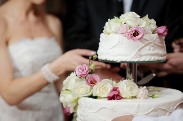 Bride and groom cutting a tiered wedding cake decorated with flowers.