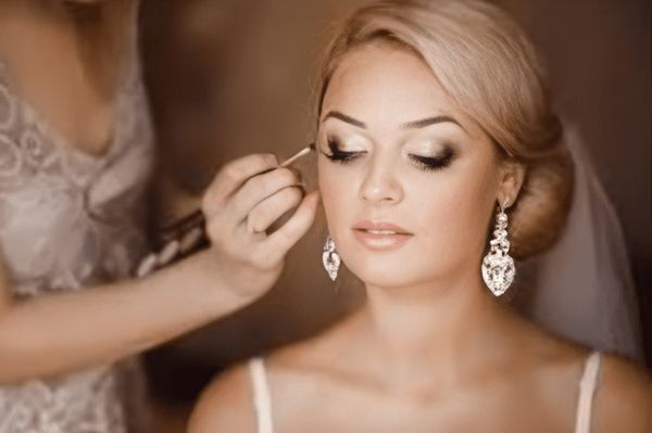 Bride having makeup applied, wearing a veil and earrings. Makeup artist at work.