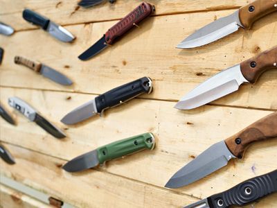 A bunch of knives are hanging on a wooden wall.