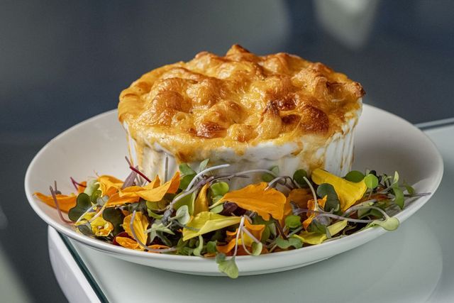 Baked savory pie in a white bowl on mixed greens salad, with a golden crust
