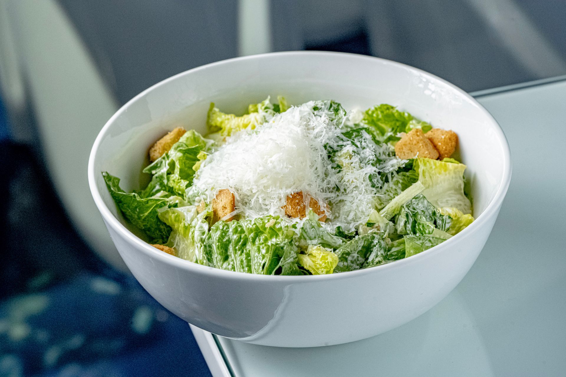 Caesar salad in a white bowl topped with grated cheese and croutons