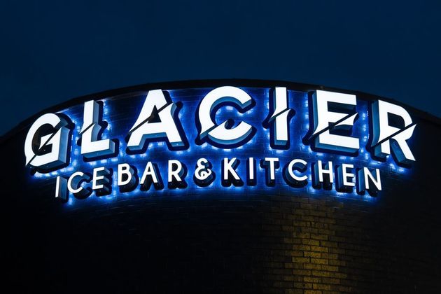 Glacier Ice Bar & Kitchen illuminated sign in blue and white on a dark brick wall