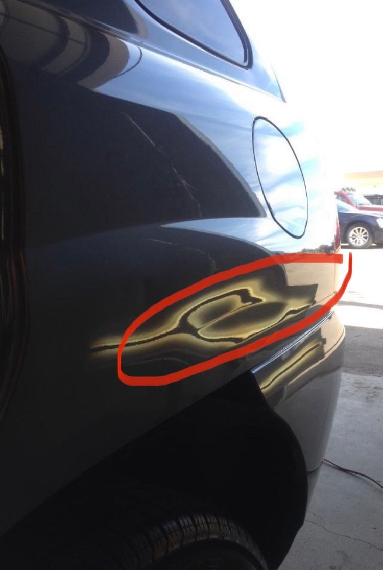 A close-up of a black car with a dent circled in red