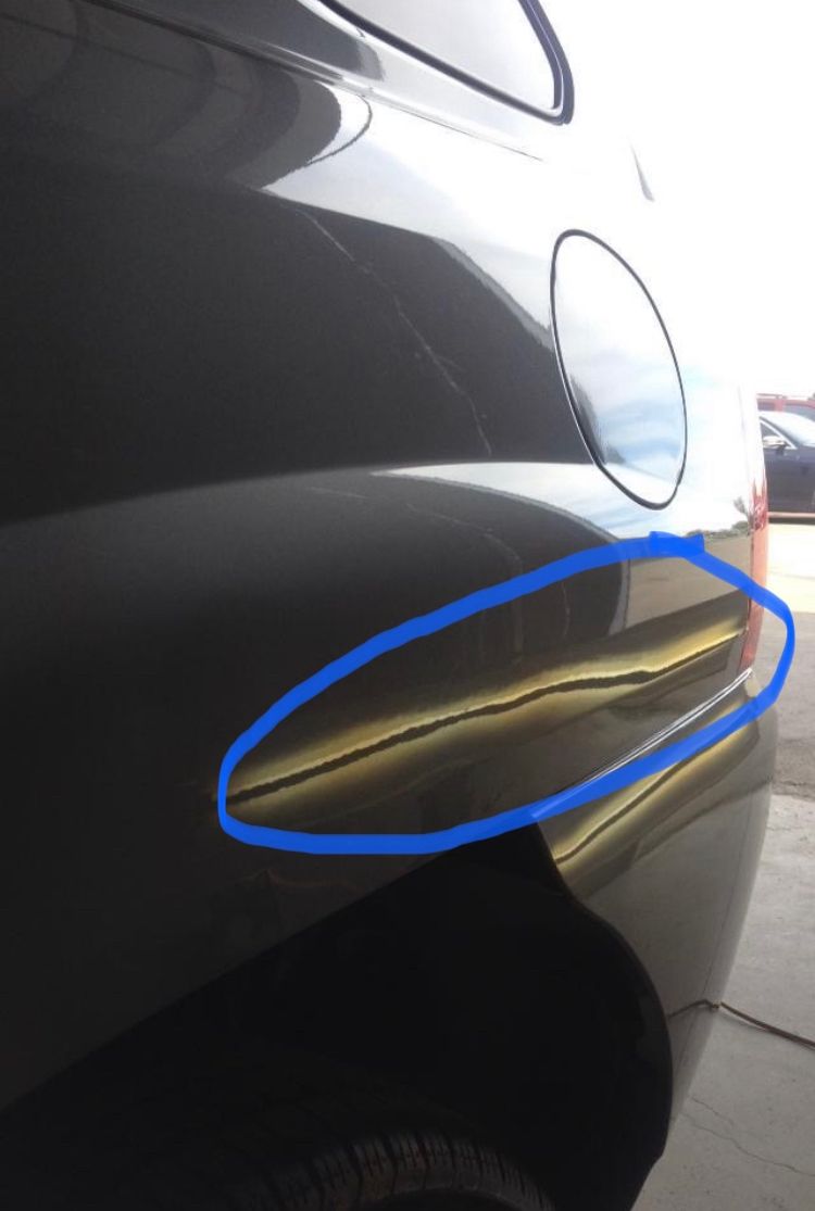 A close-up of a black car with a fixed dent circled in blue