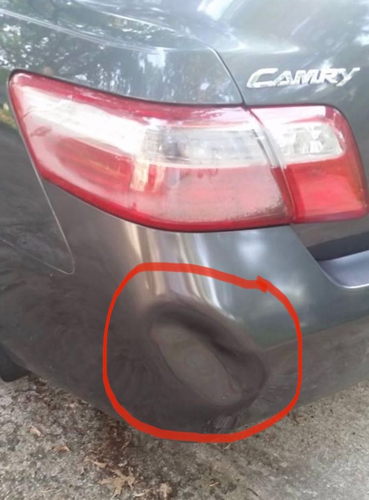 A close-up of a gray car with a dent at the back circled in red 