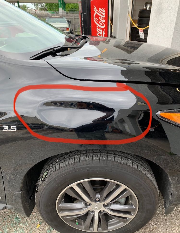 A close-up of a black car with a dent circled in red 