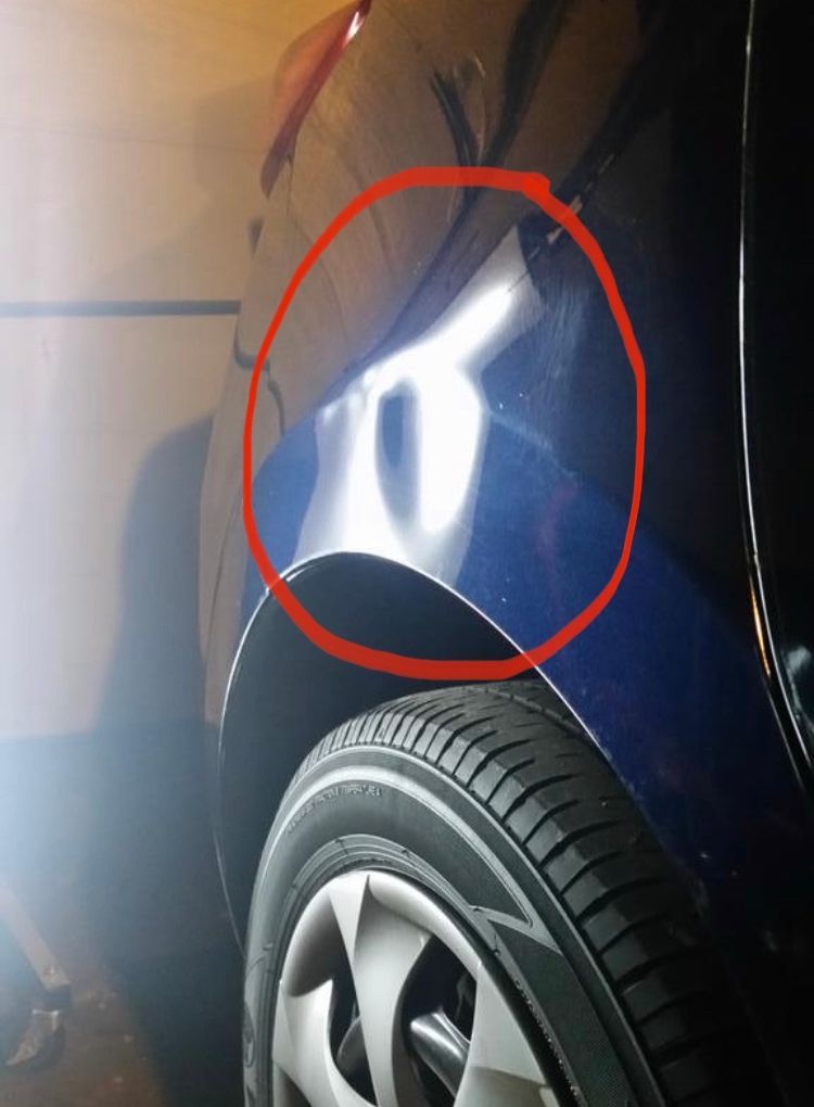 A close-up of a blue car with a dent circled in red