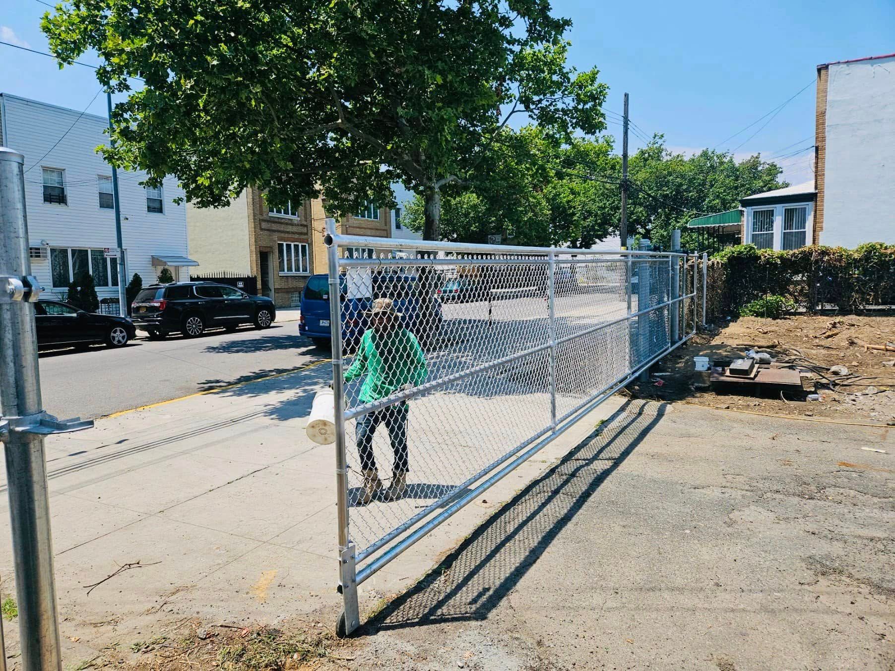 Person near open chain link gate on a paved area, street in background with cars and buildings.
