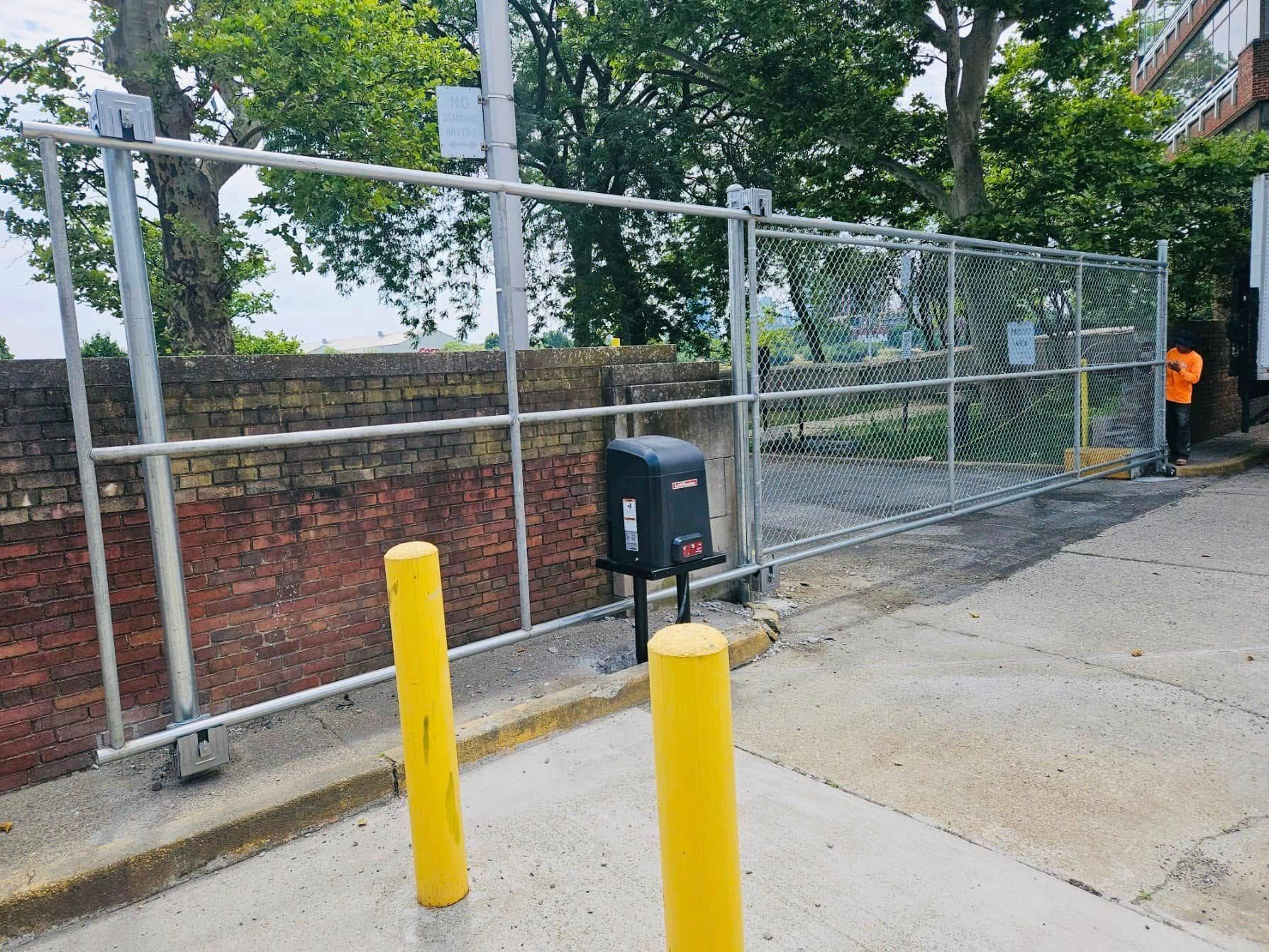 Chain link fence with automatic gate, brick wall, and yellow bollards.