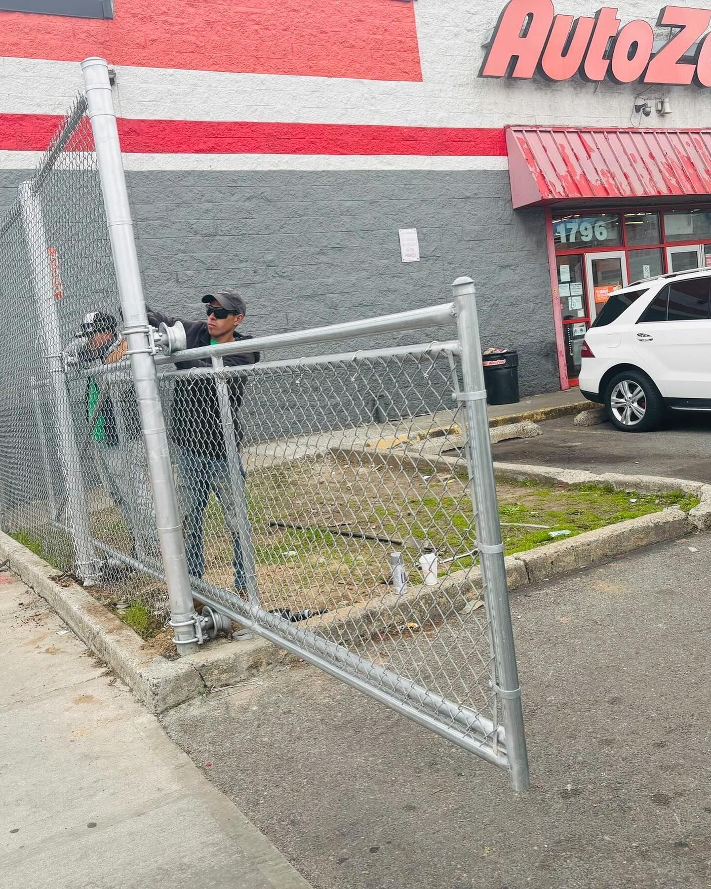 Two people working on a chain-link fence in front of an AutoZone store.