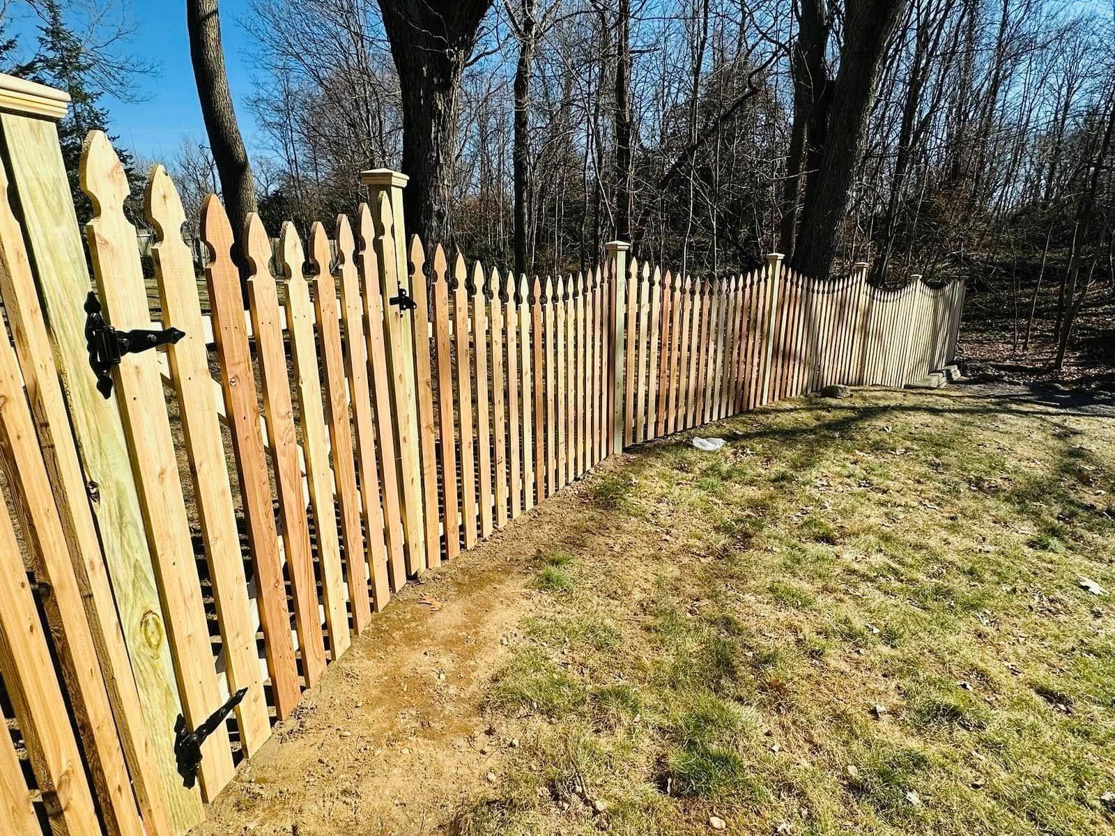 Wooden picket fence in a sunny grassy yard with trees in the background.
