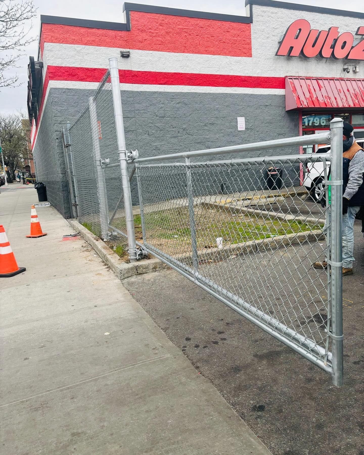 Chain-link fence leaning away from AutoZone building. Orange cones on sidewalk.