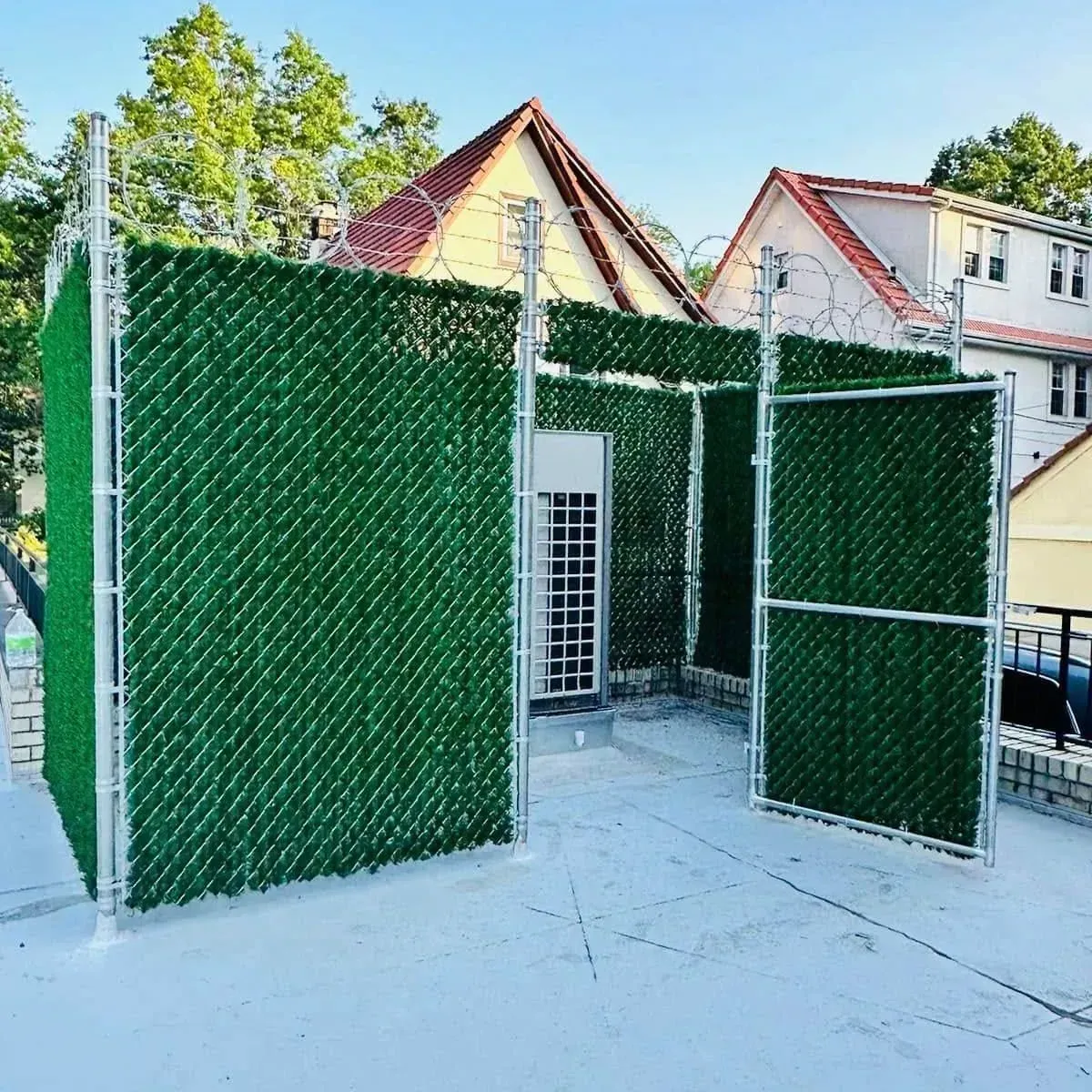 Green chain link fence structure on a rooftop. Houses and trees are in the background, daytime.