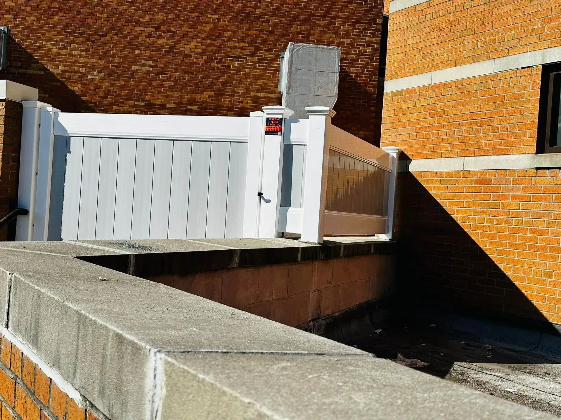White fence on a brick building's edge. Concrete ledge in foreground.