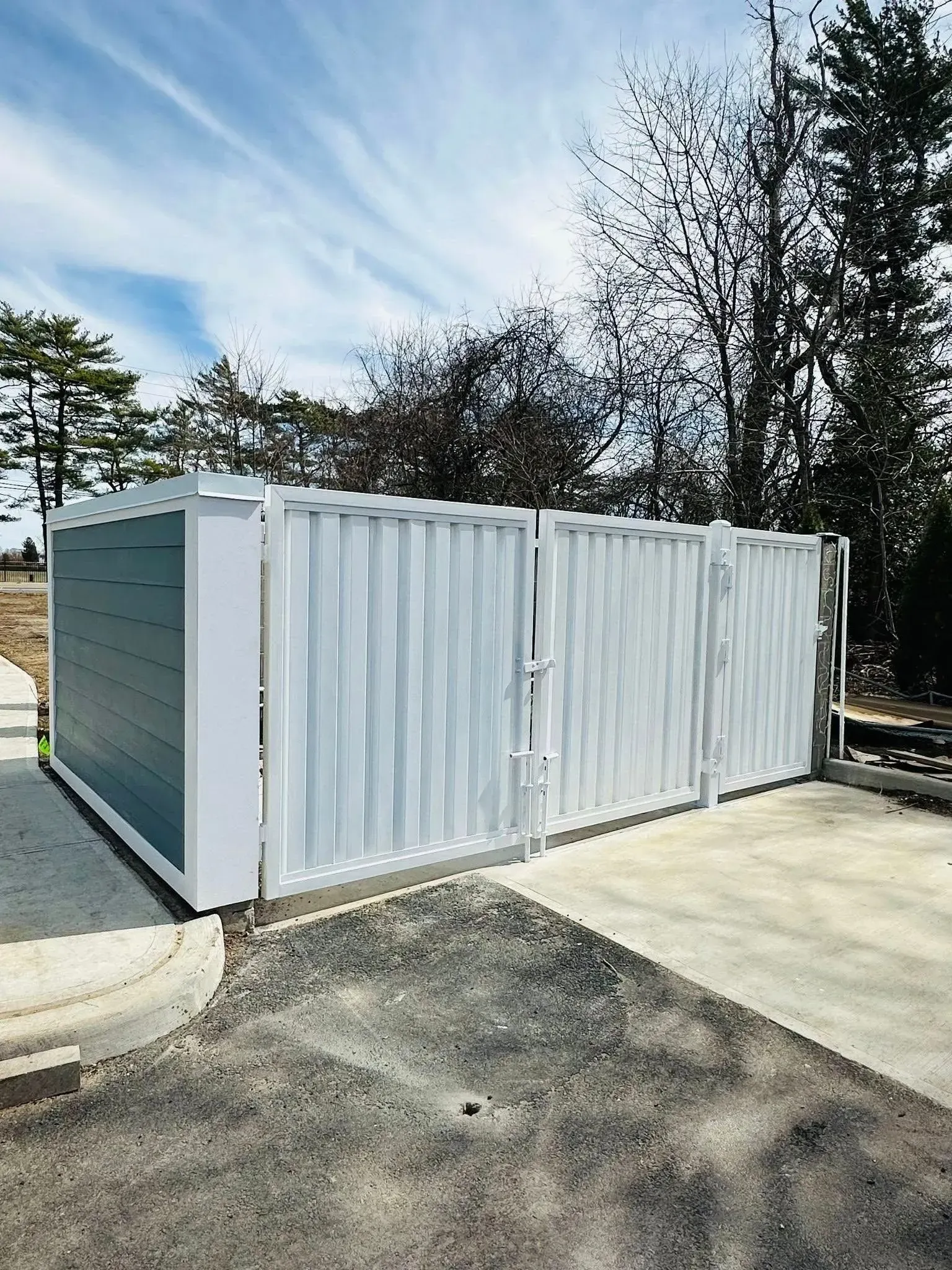 White metal enclosure with gated entrance outdoors, green-gray side panel, sunny day.