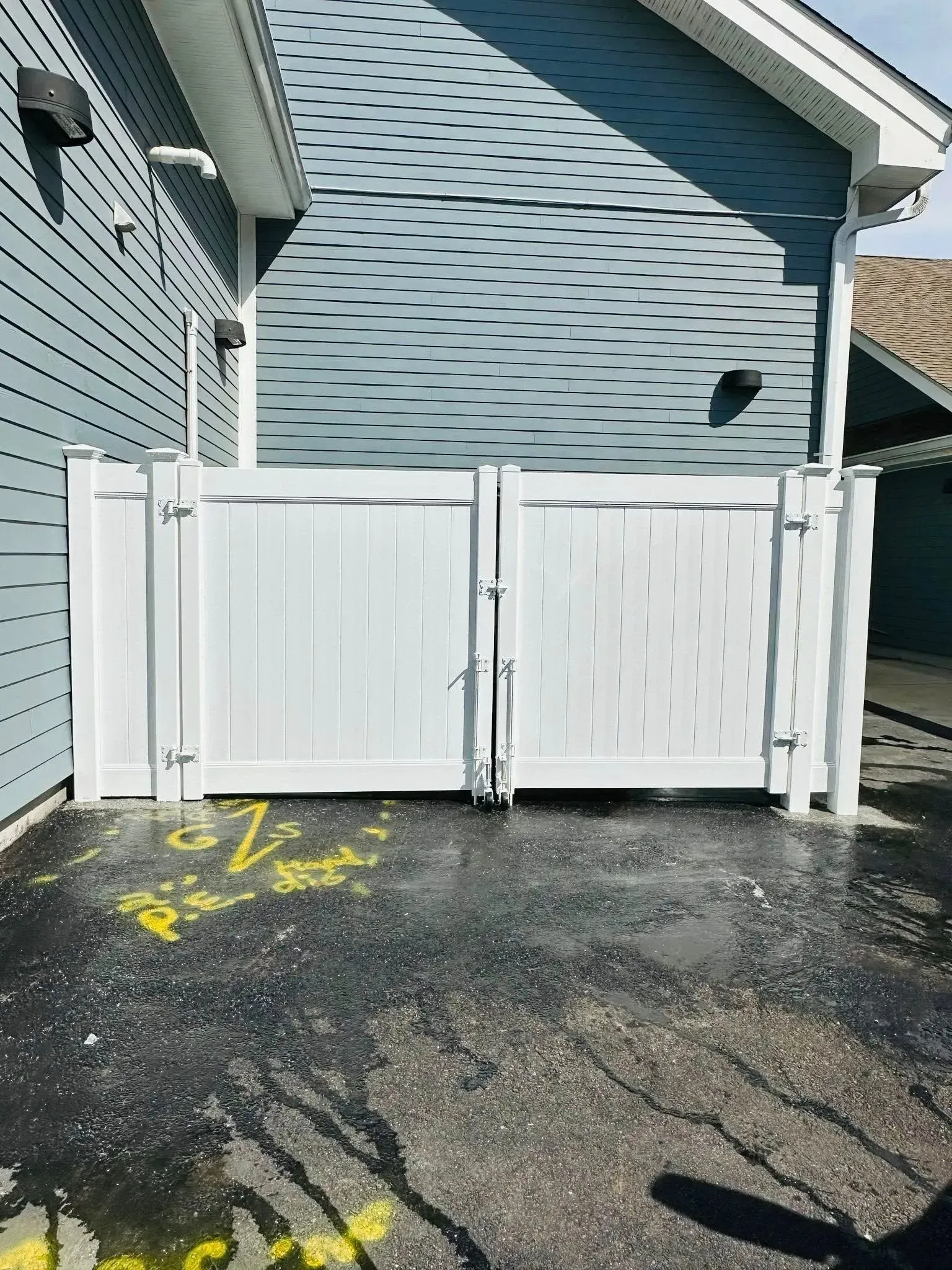 White double gate in front of a blue building. Black pavement with yellow markings.