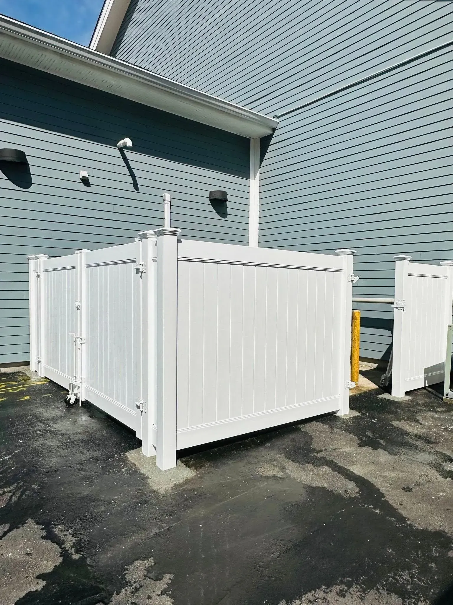 White vinyl fenced enclosure against a textured gray building.