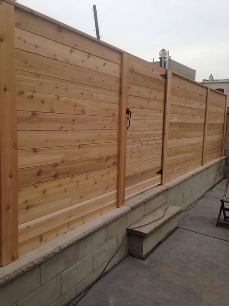 Wooden horizontal slat fence with gate, set on a concrete block foundation, in an outdoor space.