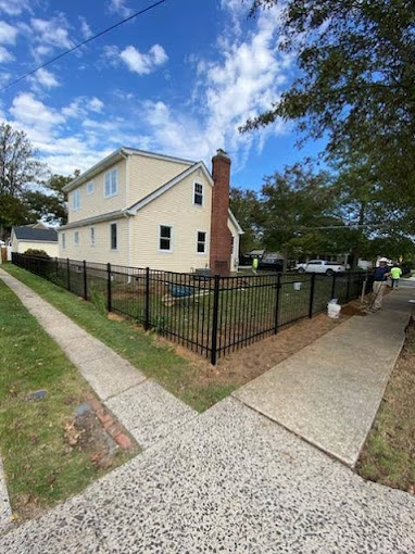 Yellow house with black fence, brown brick chimney. Sidewalks and green grass.