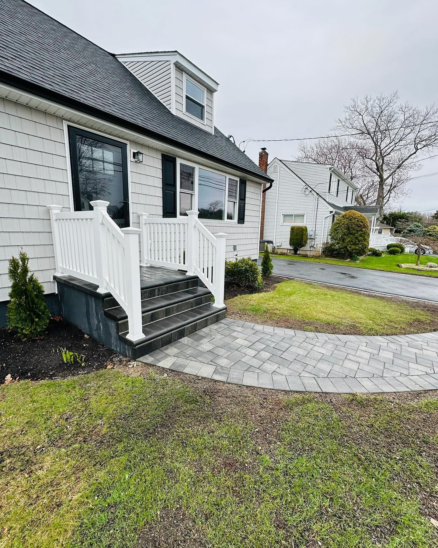 White house with white railings, grey stone steps, and a paved walkway on a cloudy day.