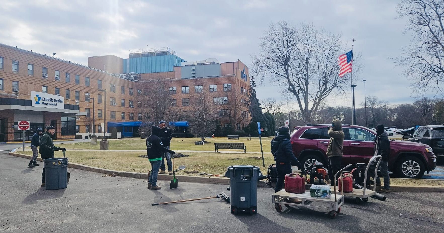 People with equipment near hospital entrance; flag and vehicles visible.