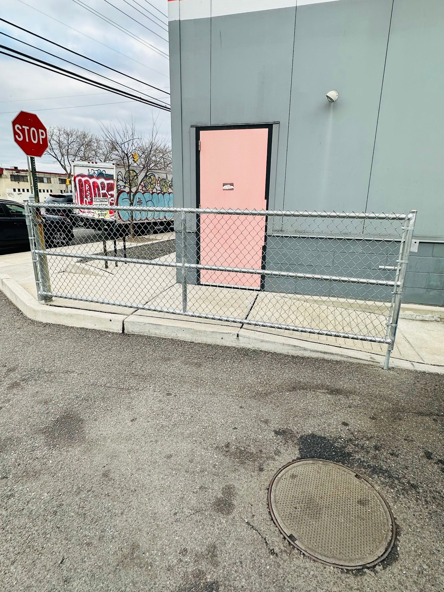 A stop sign, building with pink door, metal railing, and gravel pavement.
