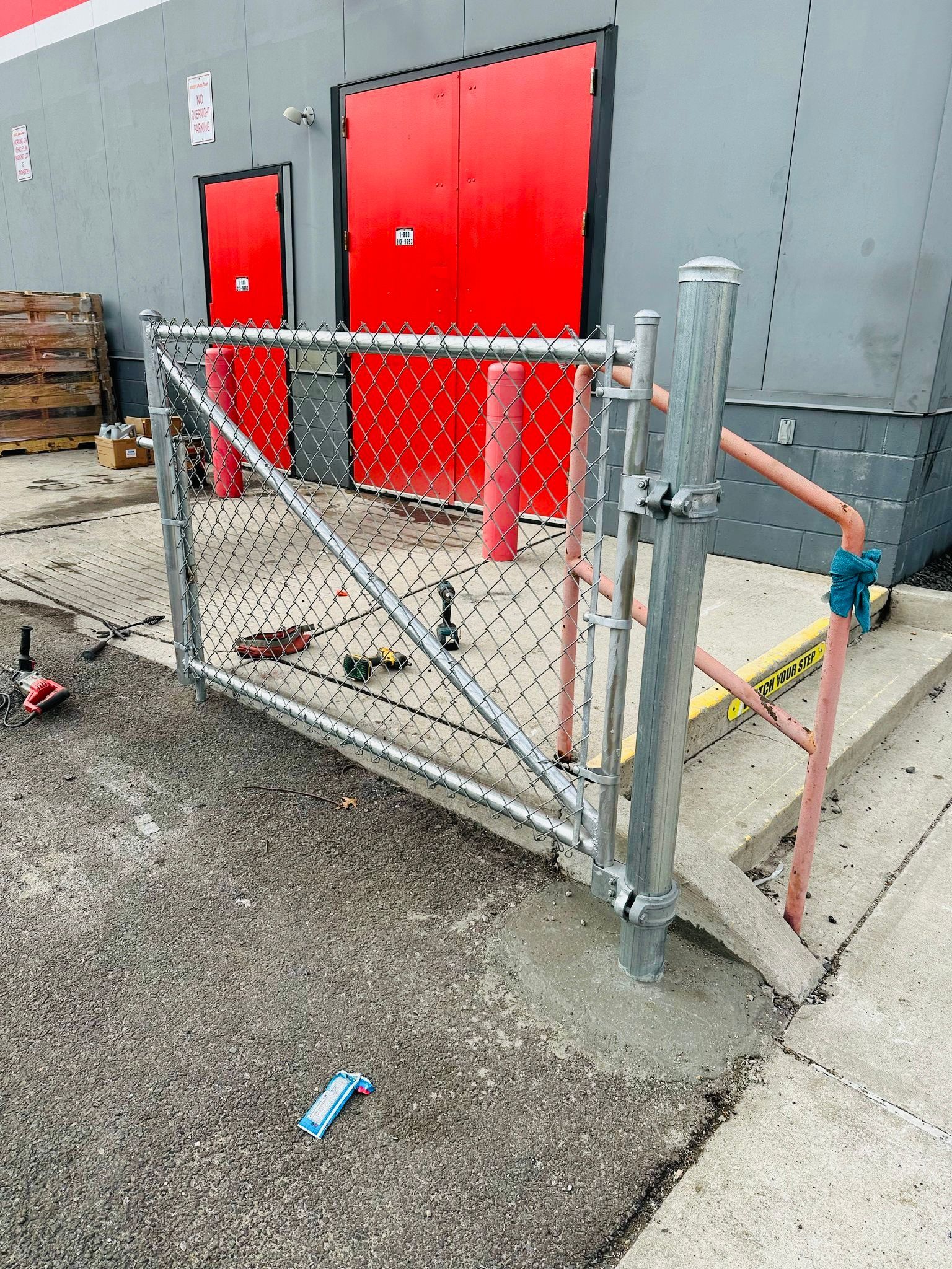 A chain-link fence gate installed at a loading dock with red doors in the background.