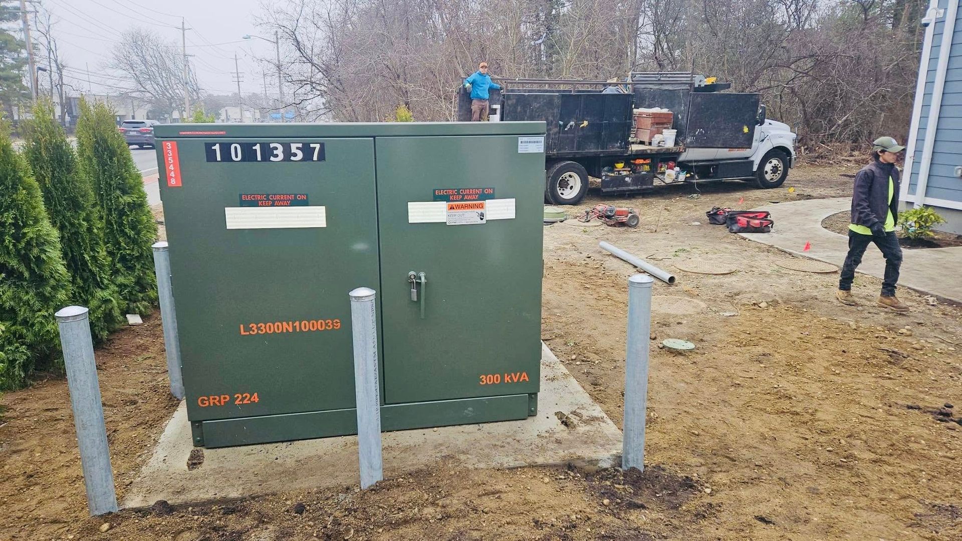 Green electrical box outside with workers and a truck.