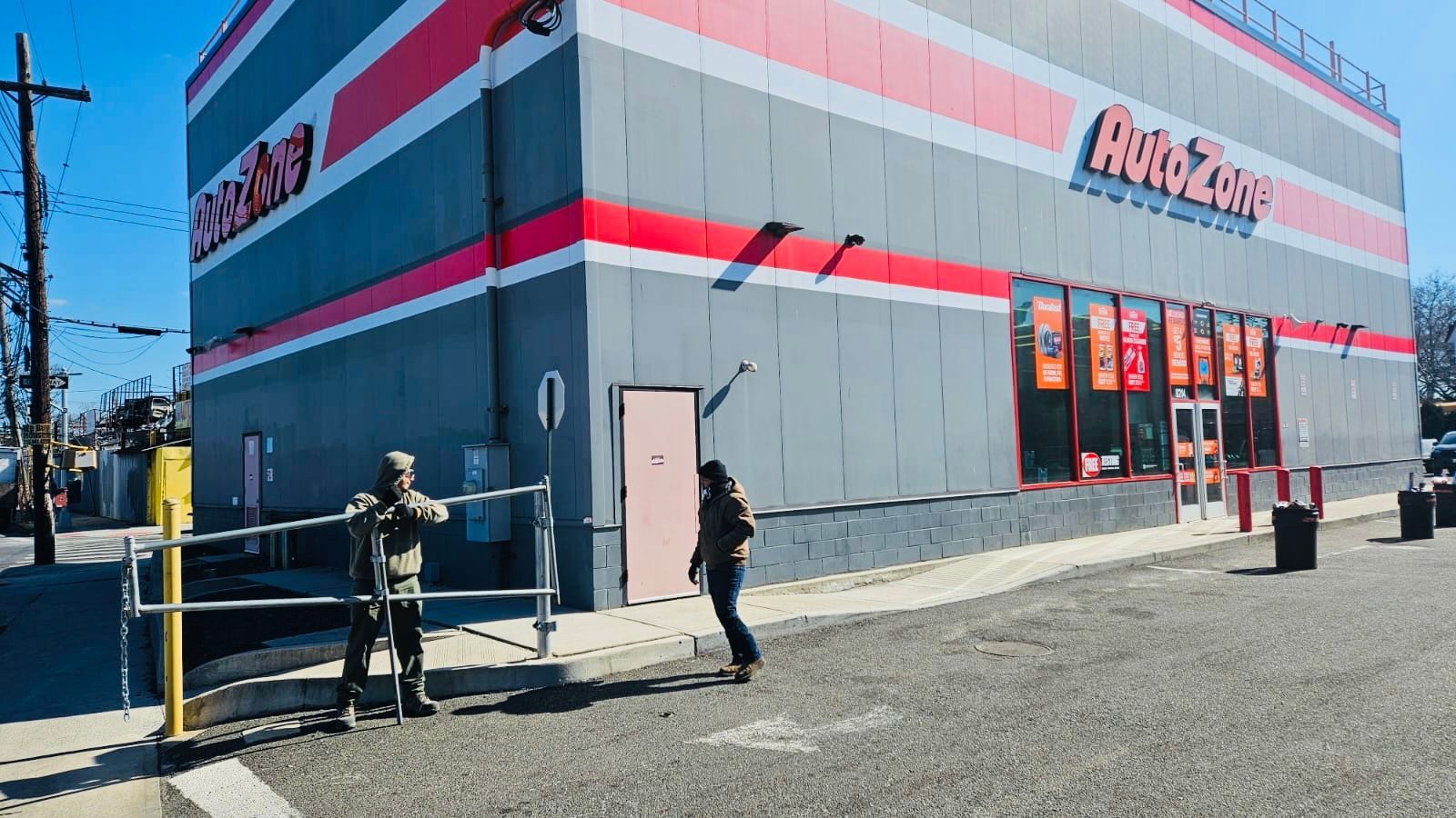AutoZone store exterior; two people by a fence; sunny day.