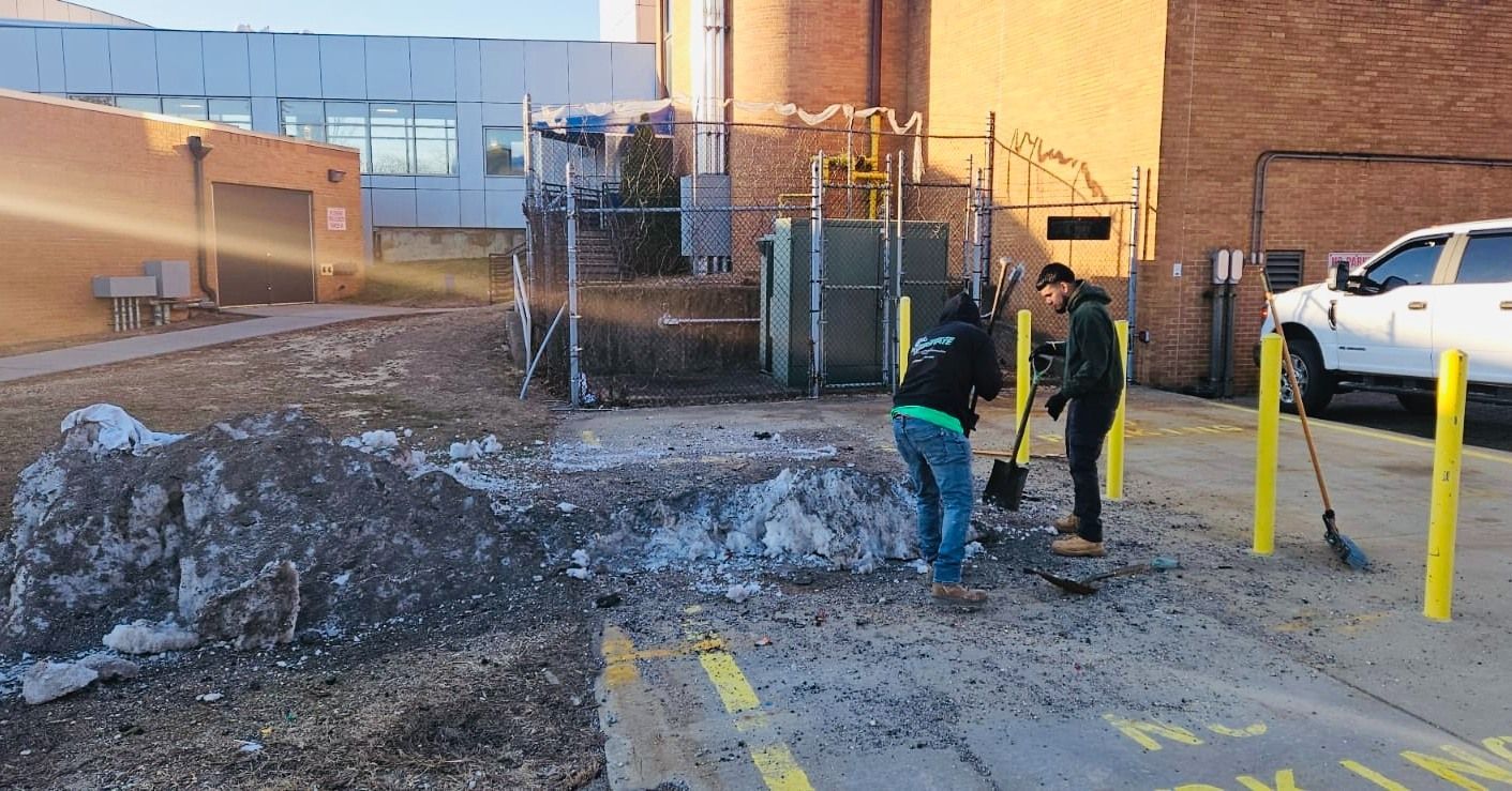 Two people shoveling debris in front of a building with a pickup truck nearby.