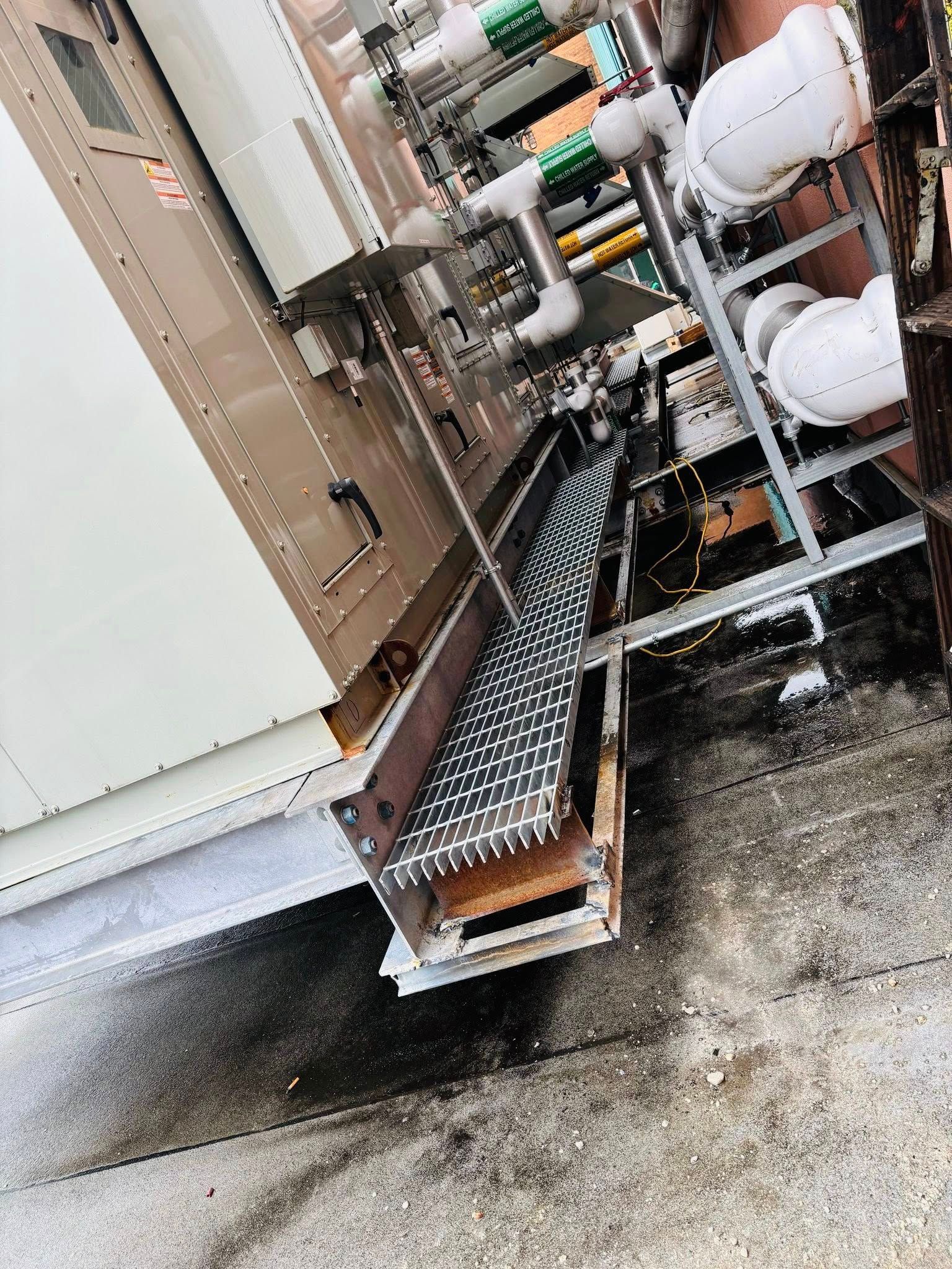 Metal grating on a structure next to pipes and a beige industrial panel.