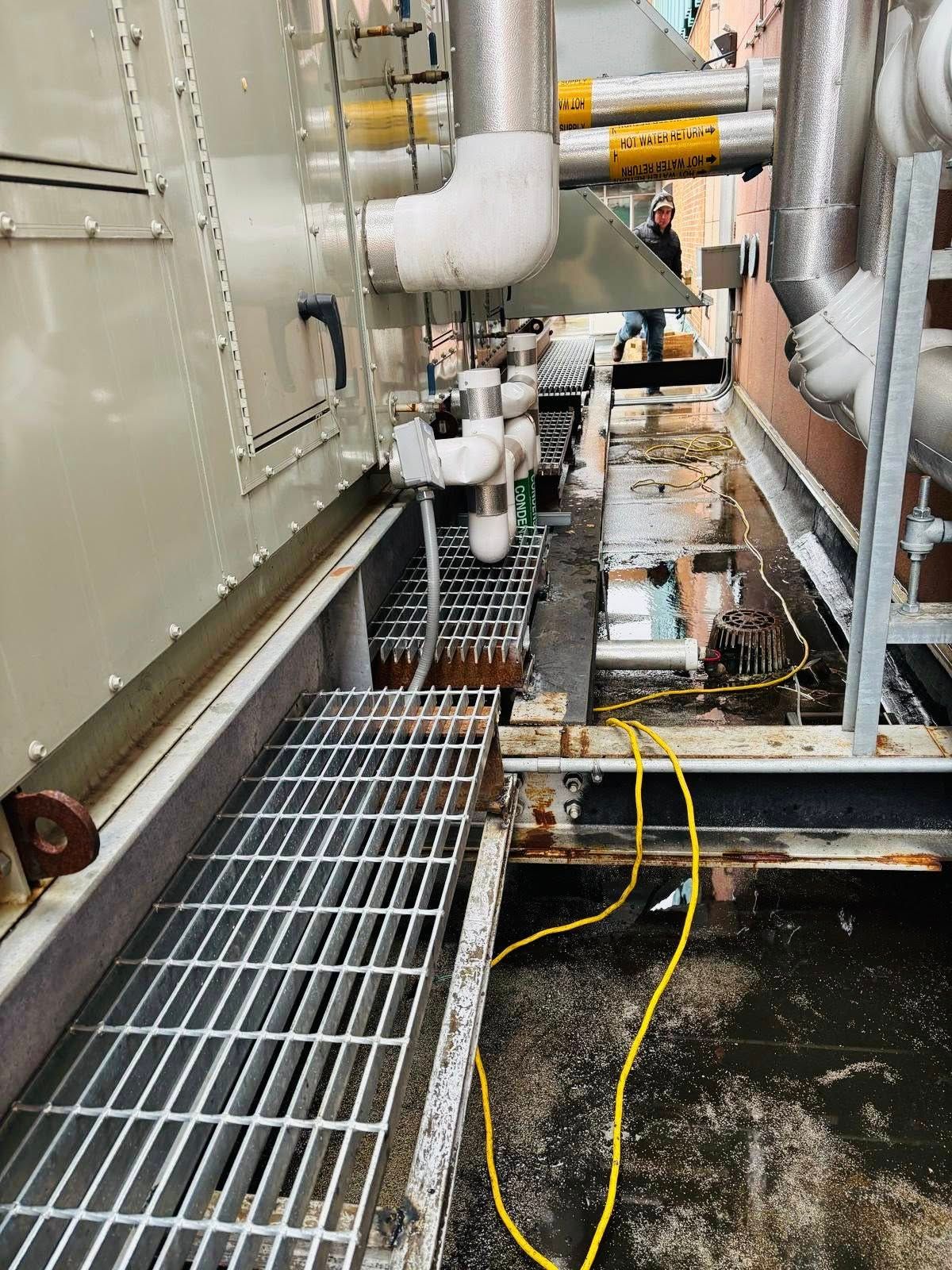Industrial rooftop with metal grating, pipes, and electrical wiring.
