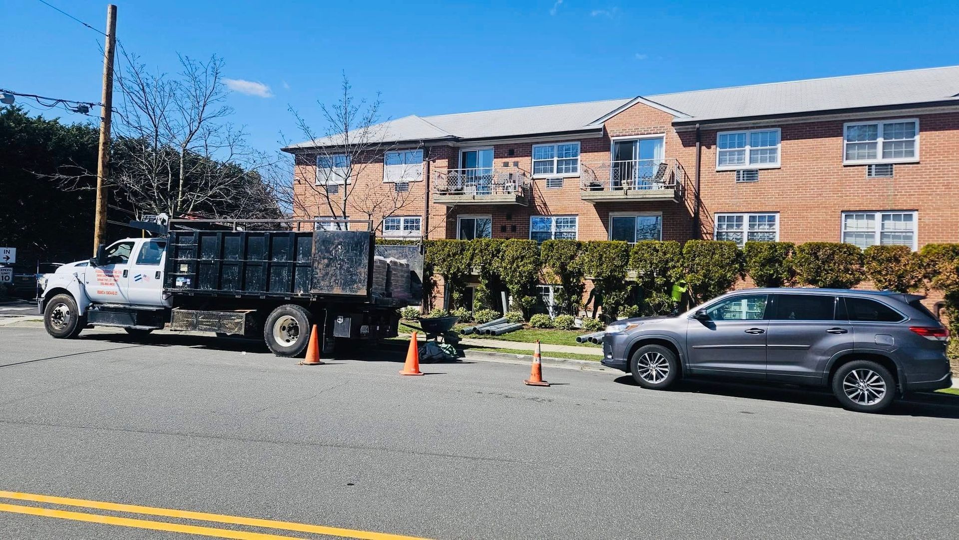 Dump truck and grey SUV parked on street with orange cones, in front of brick apartment building.