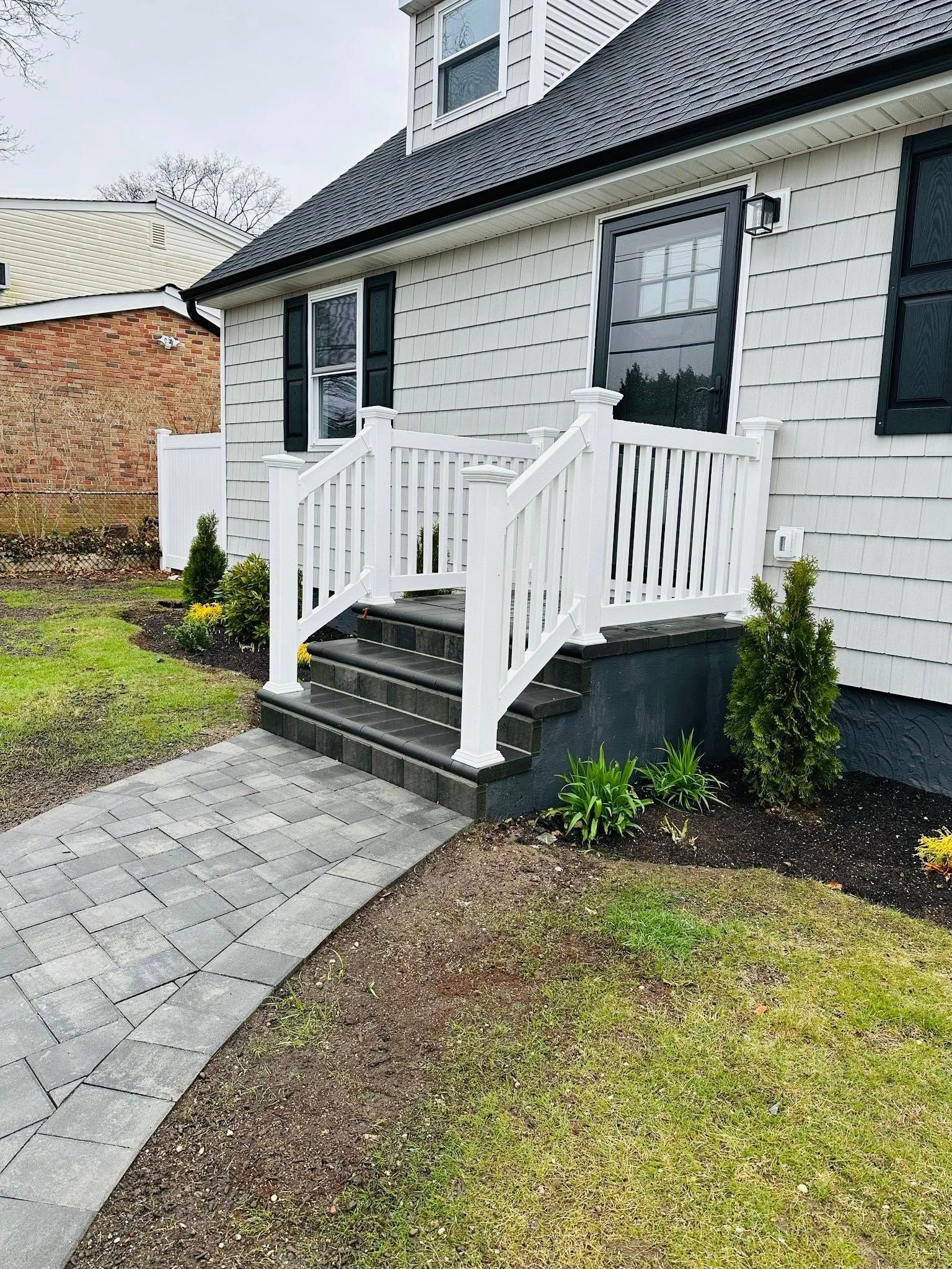 White house with white railings and a walkway. Brick building is in the background.